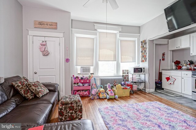 living room with cooling unit, radiator heating unit, ceiling fan, and light hardwood / wood-style floors