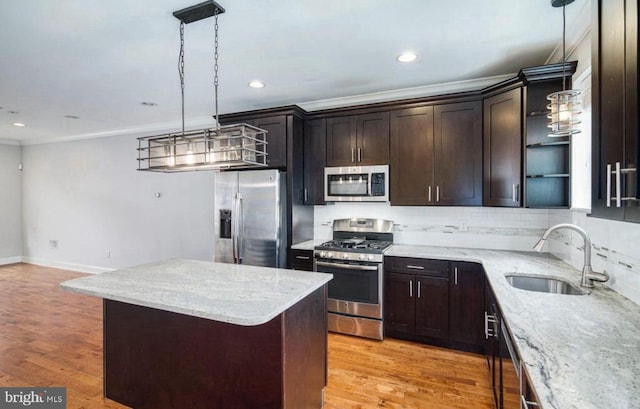 kitchen with light stone counters, sink, light hardwood / wood-style flooring, stainless steel appliances, and decorative light fixtures