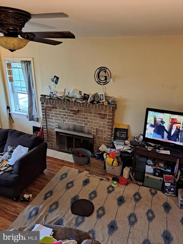 living room featuring wood-type flooring, a brick fireplace, and ceiling fan