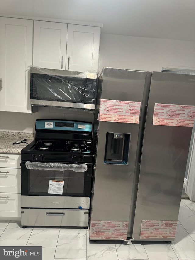 kitchen with stainless steel appliances, light stone countertops, and white cabinets