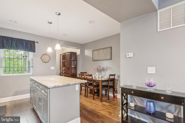 kitchen with gray cabinets, a kitchen island, pendant lighting, dark hardwood / wood-style flooring, and light stone countertops