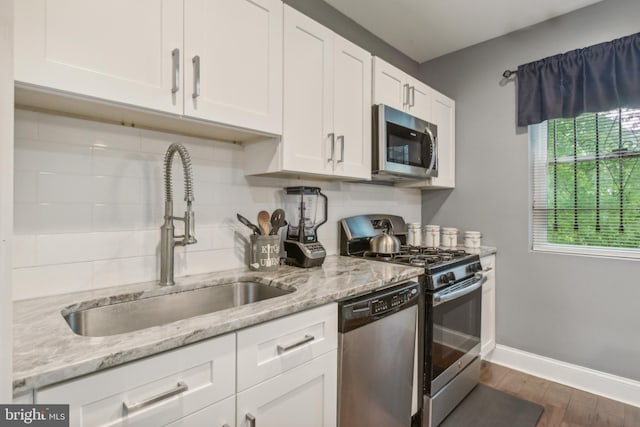 kitchen with white cabinetry, dark wood-type flooring, light stone counters, stainless steel appliances, and sink