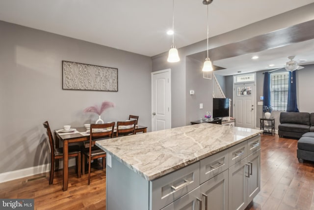 kitchen featuring hardwood / wood-style flooring, ceiling fan, hanging light fixtures, a center island, and light stone counters