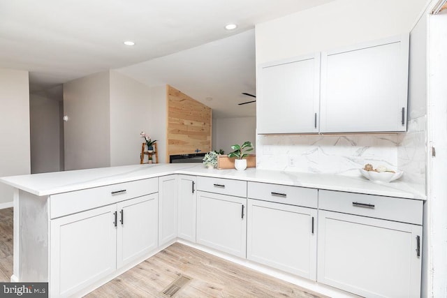 kitchen featuring white cabinets, kitchen peninsula, light hardwood / wood-style flooring, and tasteful backsplash