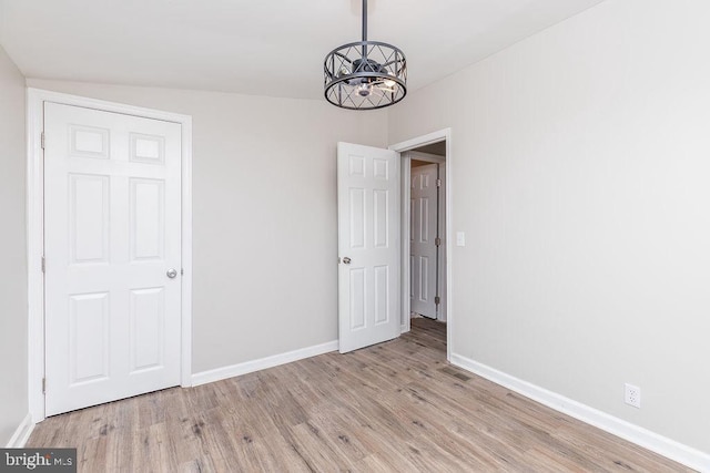 unfurnished room with lofted ceiling, light wood-type flooring, and an inviting chandelier