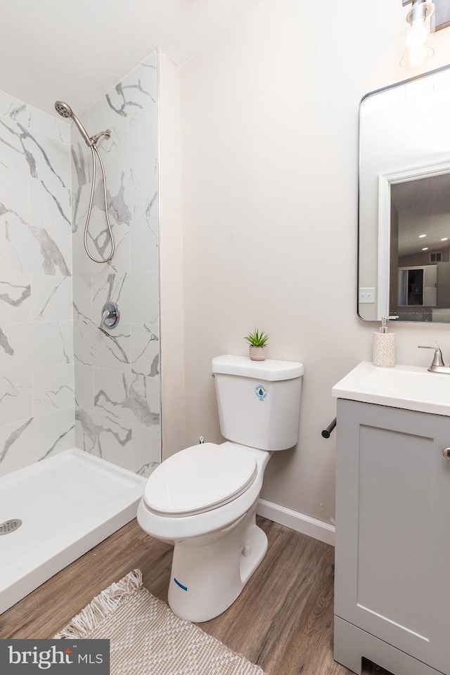 bathroom with vanity, toilet, wood-type flooring, and tiled shower