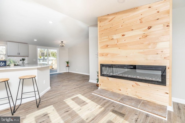 kitchen with gray cabinetry, light hardwood / wood-style floors, a kitchen bar, and backsplash