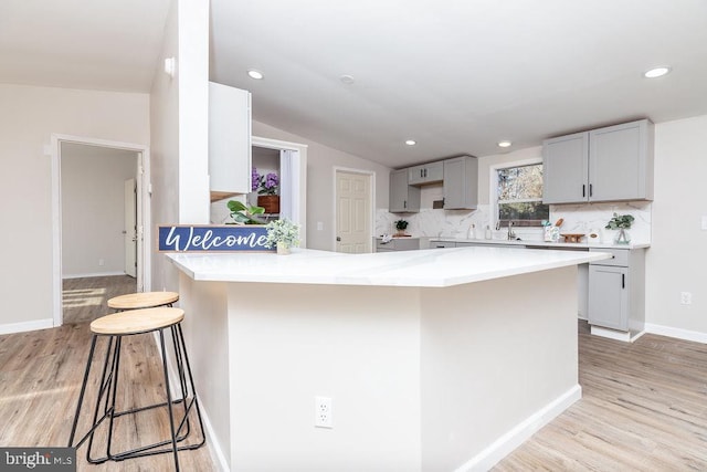 kitchen featuring a kitchen breakfast bar, light wood-type flooring, backsplash, gray cabinetry, and vaulted ceiling