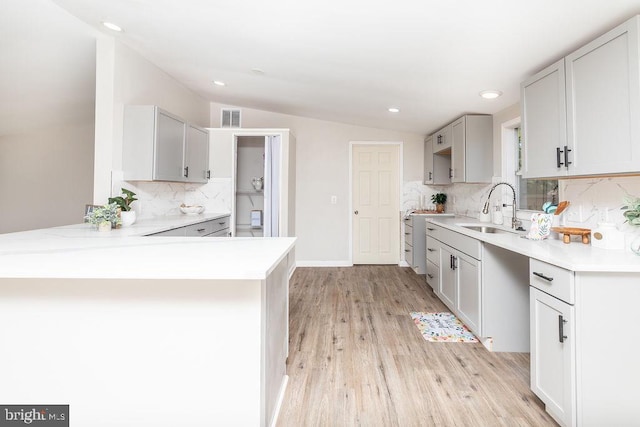 kitchen with lofted ceiling, backsplash, sink, light hardwood / wood-style flooring, and kitchen peninsula