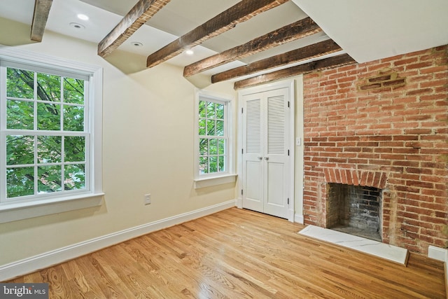 unfurnished living room with a brick fireplace, beam ceiling, and light hardwood / wood-style flooring