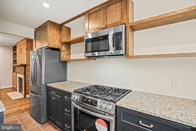 kitchen featuring stainless steel appliances, a large fireplace, light tile patterned floors, and light stone counters