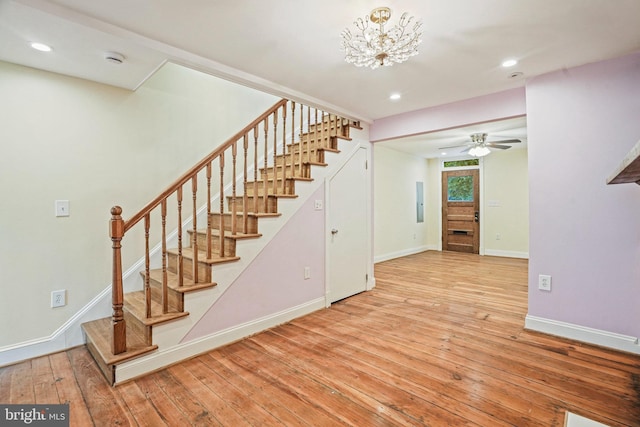 staircase with hardwood / wood-style floors and ceiling fan with notable chandelier