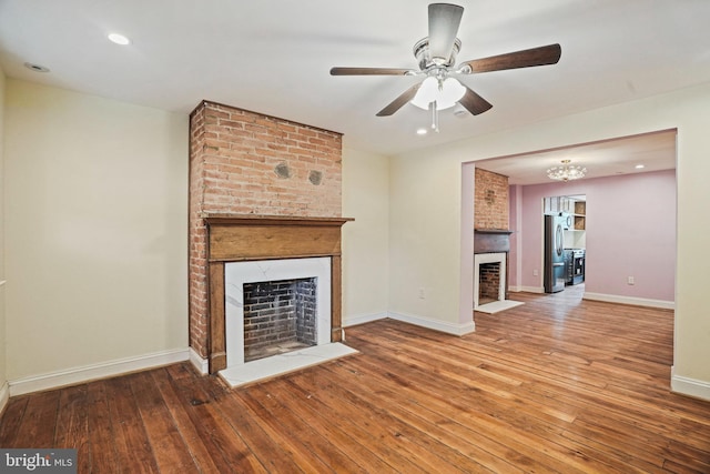 unfurnished living room featuring a brick fireplace, wood-type flooring, and ceiling fan