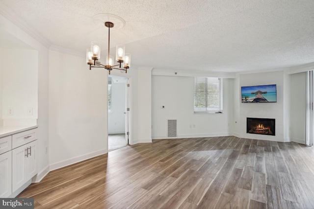 unfurnished living room with an inviting chandelier, light hardwood / wood-style flooring, ornamental molding, and a textured ceiling