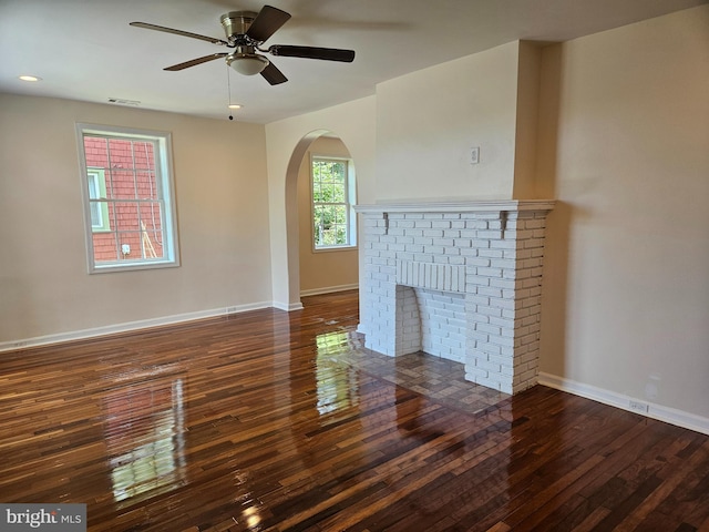 unfurnished living room featuring dark wood-type flooring, ceiling fan, and a brick fireplace