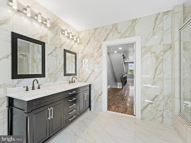 bathroom featuring marble finish floor, a shower with shower door, tile walls, and a sink