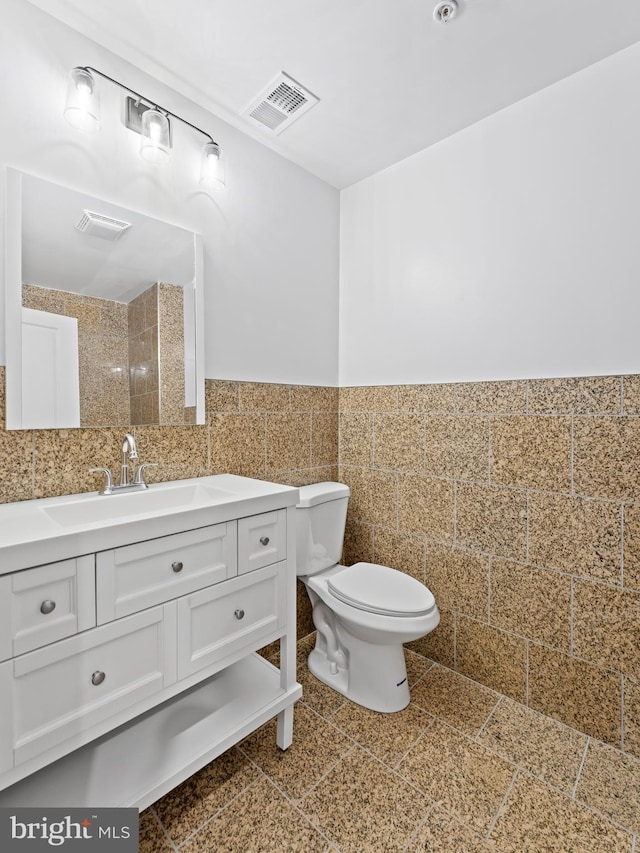 bathroom featuring vanity, a wainscoted wall, visible vents, tile walls, and toilet