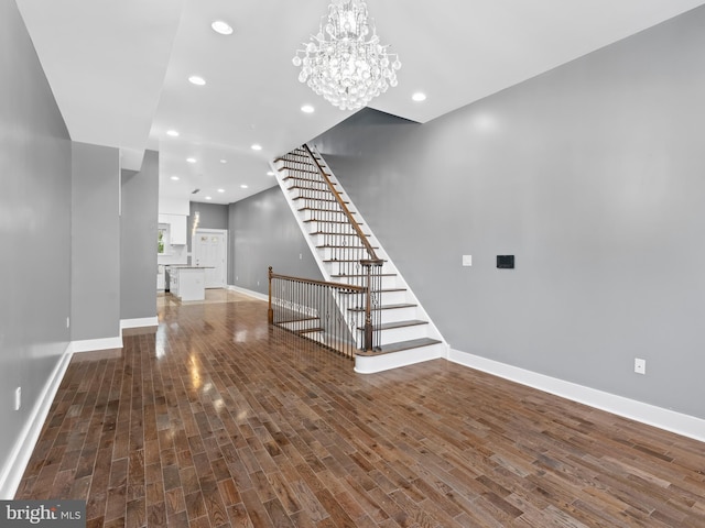 unfurnished living room featuring stairway, wood finished floors, baseboards, recessed lighting, and a chandelier