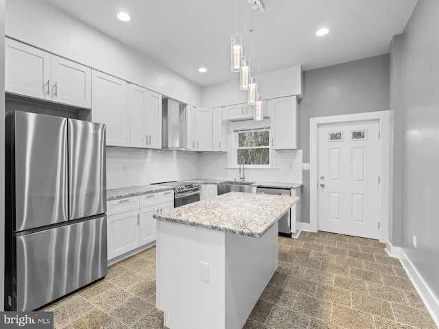 kitchen featuring decorative light fixtures, appliances with stainless steel finishes, white cabinetry, wall chimney exhaust hood, and a kitchen island