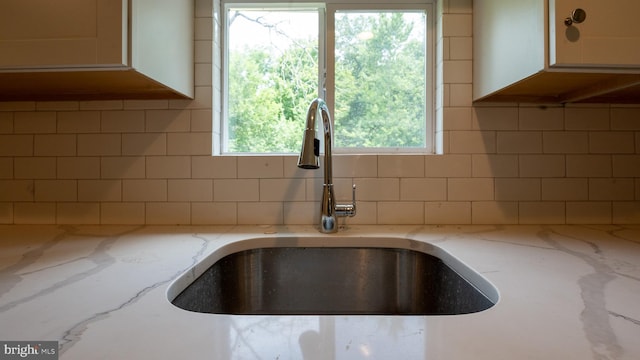 room details with white cabinetry, sink, and light stone counters