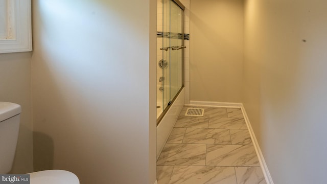 bathroom featuring toilet and bath / shower combo with glass door