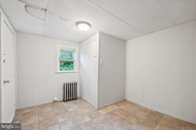 tiled spare room featuring radiator heating unit and a paneled ceiling