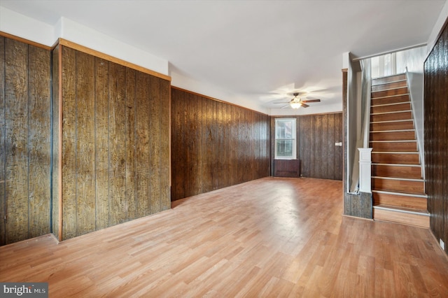 unfurnished living room with ceiling fan, wooden walls, and hardwood / wood-style flooring