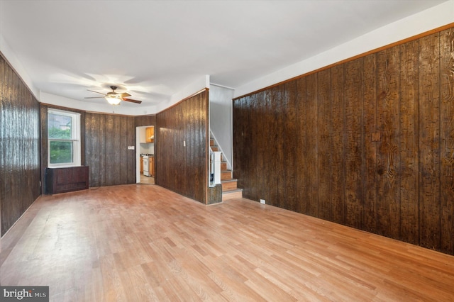 unfurnished living room with wood walls, light hardwood / wood-style flooring, and ceiling fan