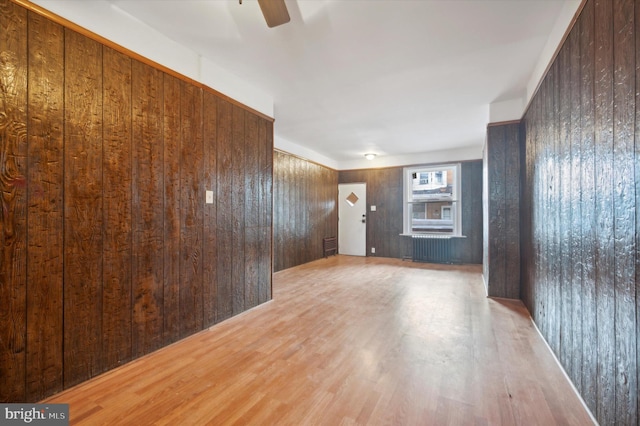 spare room with ceiling fan, light hardwood / wood-style floors, wooden walls, and radiator heating unit