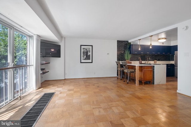 kitchen featuring decorative backsplash, a center island with sink, a breakfast bar area, light parquet flooring, and blue cabinetry