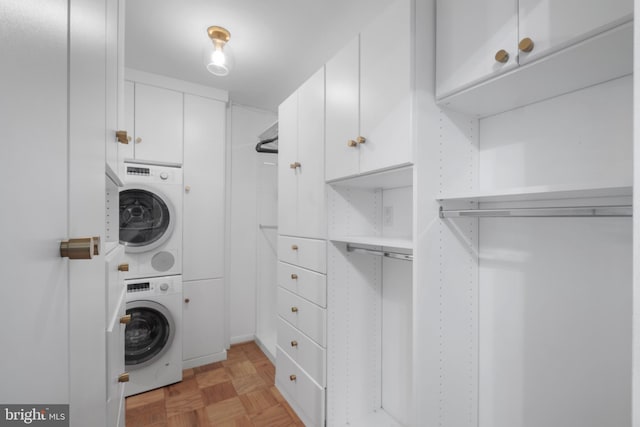 laundry room with stacked washing maching and dryer, light parquet flooring, and cabinets