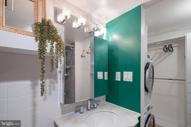 bathroom with a tile shower, stacked washer and dryer, and vanity