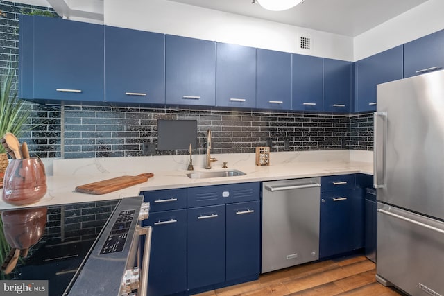 kitchen featuring decorative backsplash, light hardwood / wood-style flooring, stainless steel appliances, sink, and blue cabinets