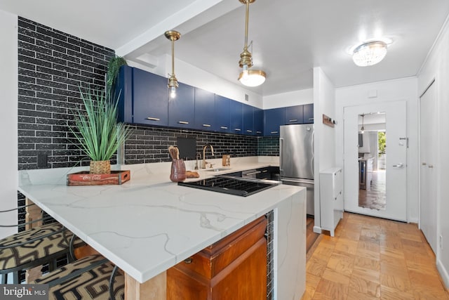 kitchen with tasteful backsplash, light stone counters, pendant lighting, blue cabinetry, and stainless steel refrigerator