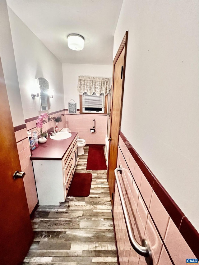 bathroom with hardwood / wood-style flooring, toilet, vanity, and tile walls