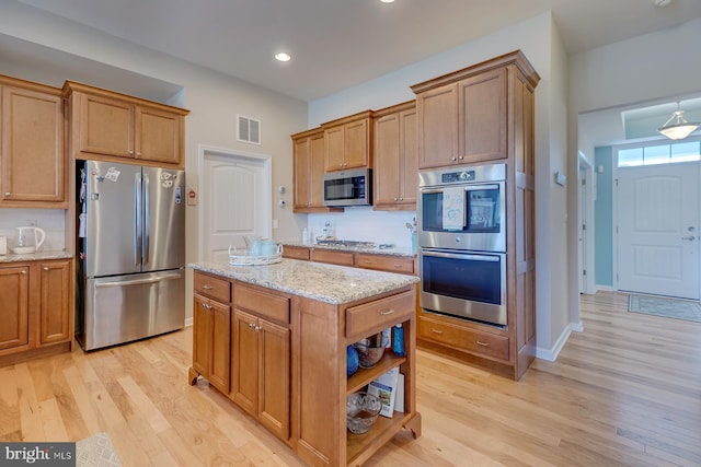 kitchen with tasteful backsplash, a center island, light hardwood / wood-style floors, light stone countertops, and appliances with stainless steel finishes