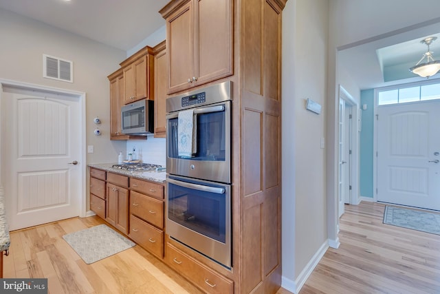 kitchen featuring light hardwood / wood-style flooring, stainless steel appliances, light stone counters, pendant lighting, and backsplash