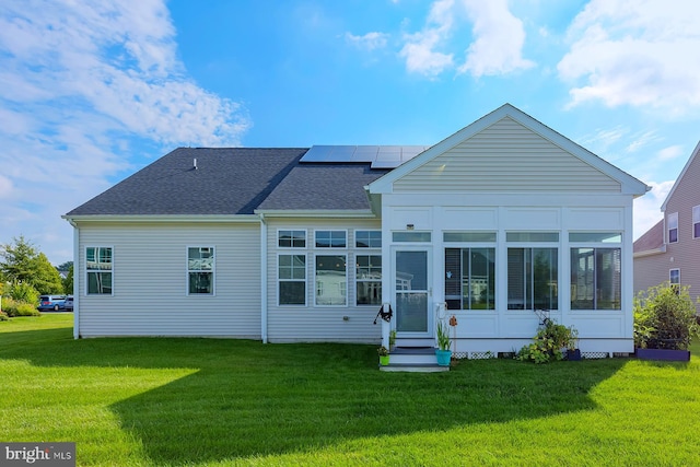 rear view of house with solar panels, a sunroom, and a lawn