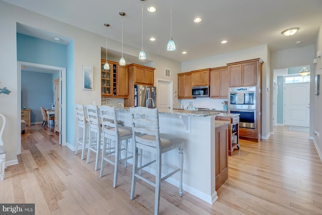 kitchen with a breakfast bar area, stainless steel appliances, decorative backsplash, light wood-type flooring, and light stone countertops