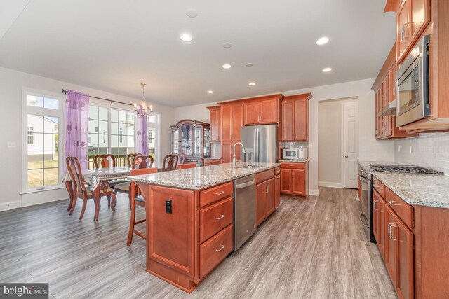 kitchen featuring light hardwood / wood-style flooring, backsplash, light stone counters, a kitchen island with sink, and stainless steel appliances