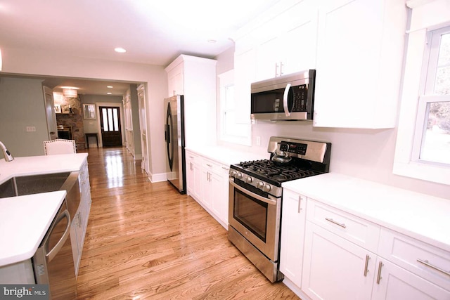 kitchen with appliances with stainless steel finishes, sink, white cabinets, and light hardwood / wood-style flooring