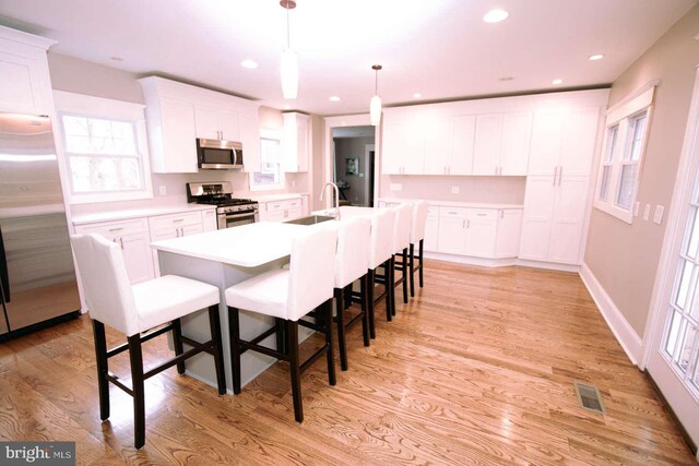 kitchen with light hardwood / wood-style floors, appliances with stainless steel finishes, white cabinets, and a kitchen island with sink