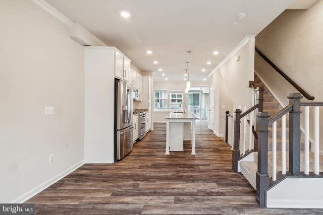 kitchen featuring a breakfast bar area, appliances with stainless steel finishes, a kitchen island with sink, white cabinets, and decorative light fixtures