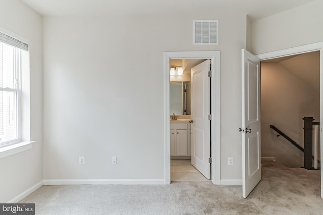 unfurnished bedroom with light colored carpet, ensuite bathroom, sink, and multiple windows