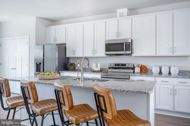 kitchen with a kitchen island with sink, a breakfast bar, white cabinets, and appliances with stainless steel finishes