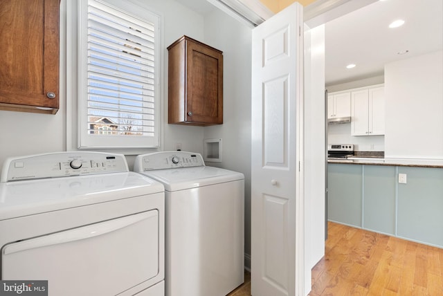 laundry area featuring washing machine and dryer, light hardwood / wood-style floors, and cabinets