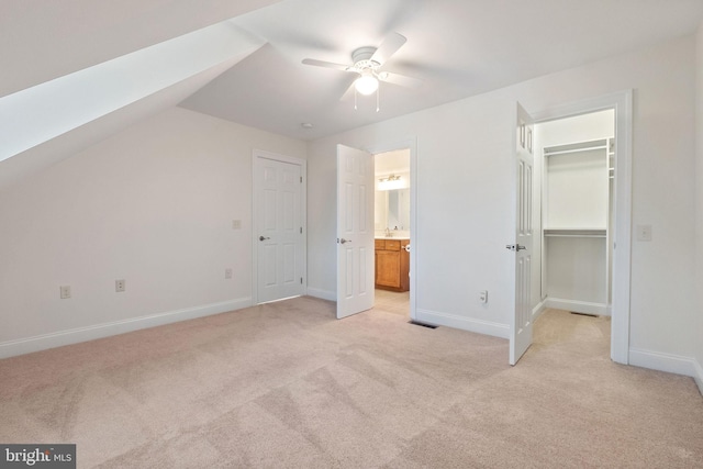 unfurnished bedroom featuring ceiling fan, a closet, vaulted ceiling with skylight, a walk in closet, and light colored carpet