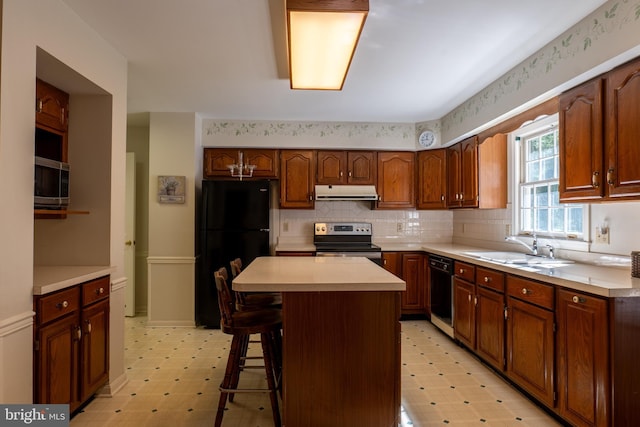 kitchen with light floors, light countertops, a sink, under cabinet range hood, and black appliances