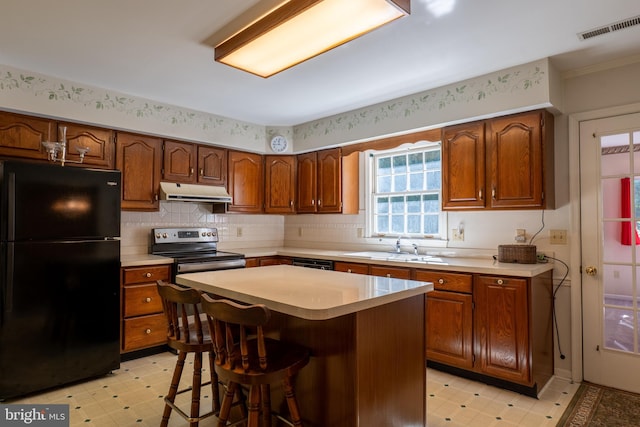 kitchen with light floors, light countertops, under cabinet range hood, and black appliances