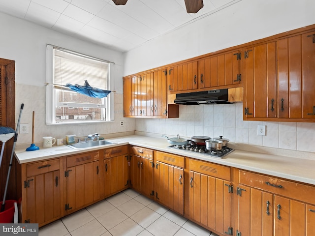 kitchen featuring light tile patterned flooring, stainless steel gas stovetop, sink, backsplash, and ceiling fan